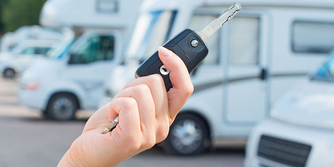 Hand holding RV key with multiple RVs on a dealership lot in the background